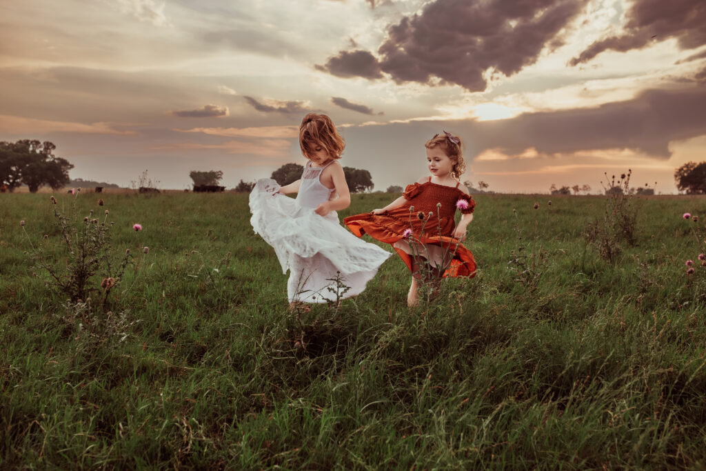 lifestyle family photograph of two young girls twirling in a scenic farm field in dresses
