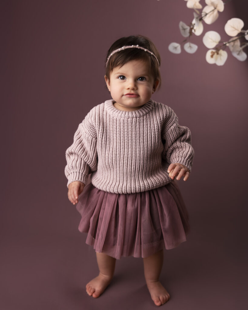 image from bellevue childhood photographer, Telly Dez Photography, of an early walker child standing on a monotone mauve backdrop