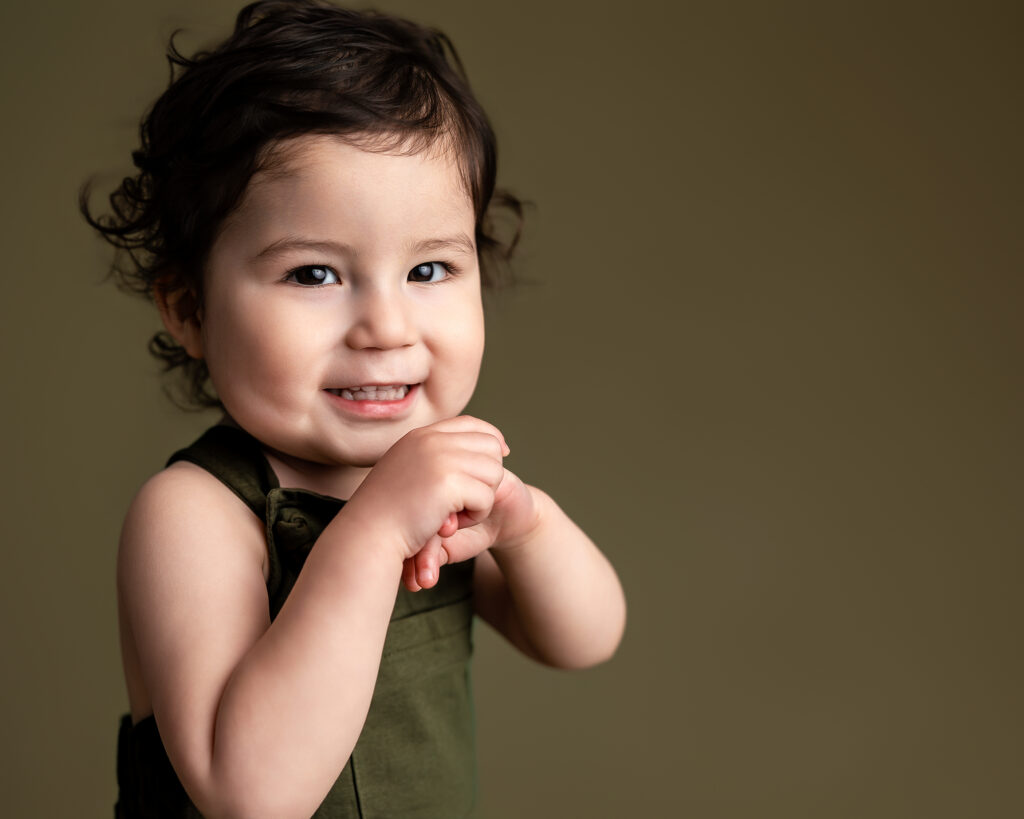 image from bellevue childhood photographer, Telly Dez Photography, of a young boy smiling on olive green backdrop.
