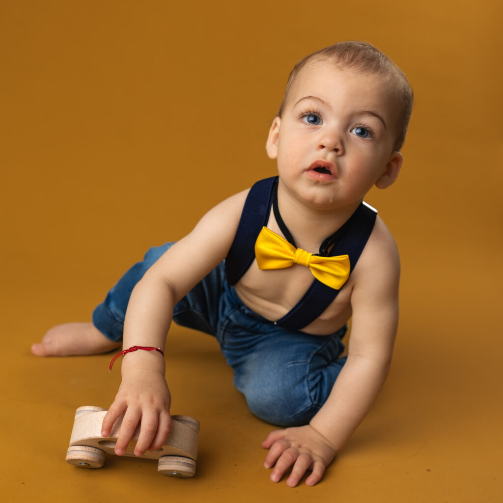 young boy playing with a toy car in a yellow bowtie