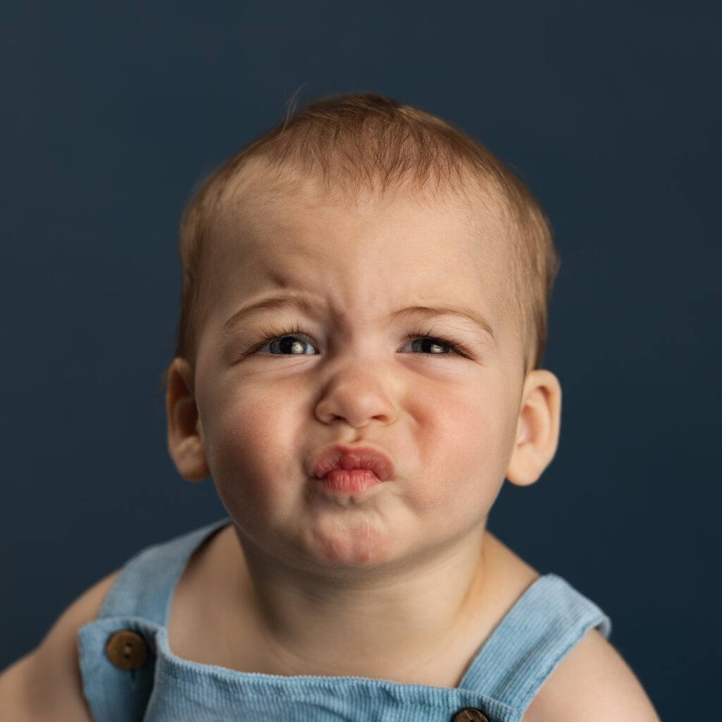 personality portrait of a young boy frowning and looking concerned on a blue backdrop