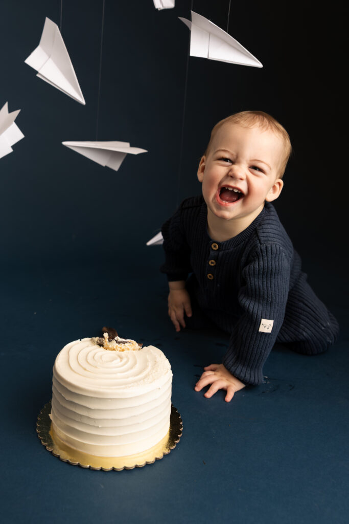 young boy laughing with a white cake as white paper airplanes fly behind him