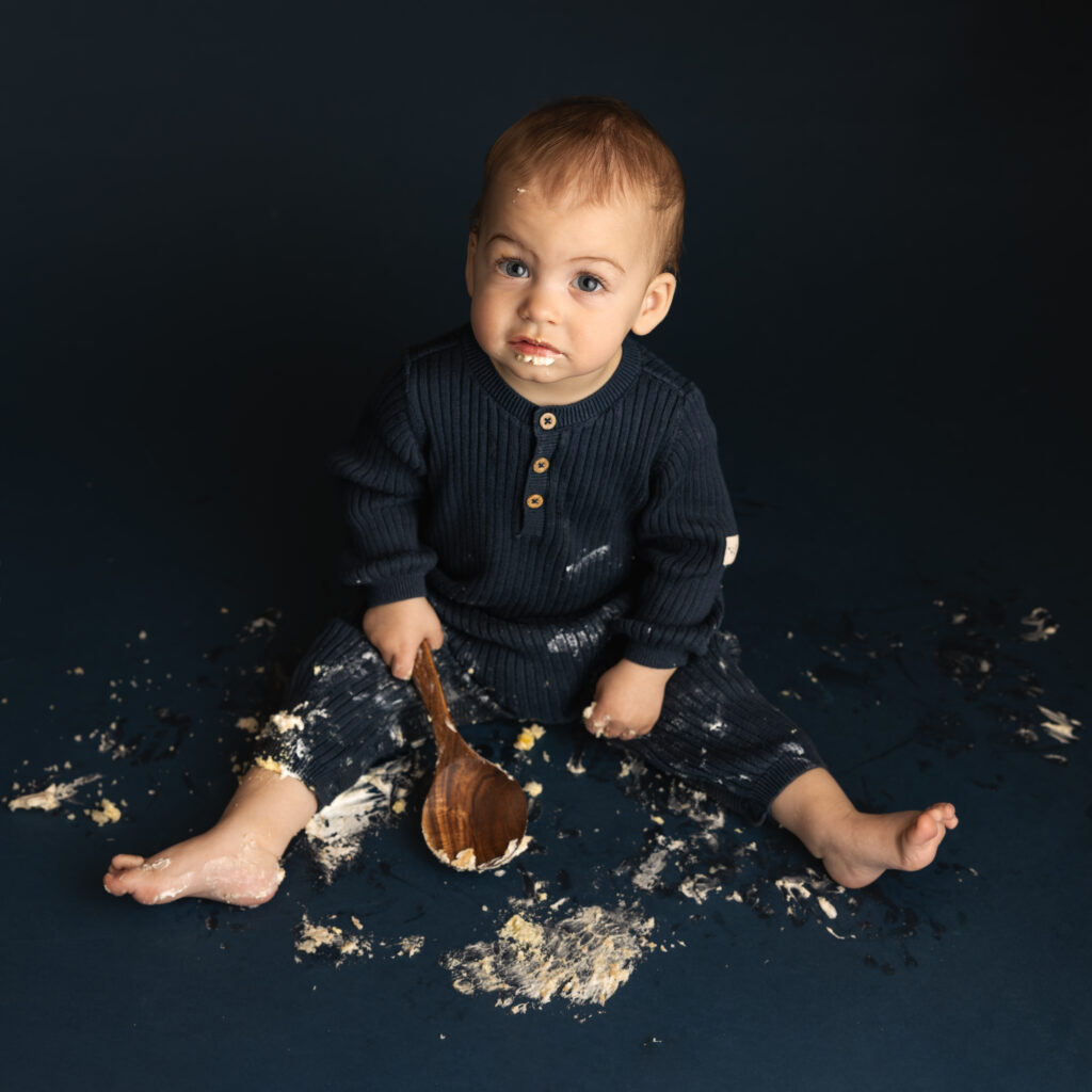 cake smash image of a little boy with a wooden spoon covered in frosting