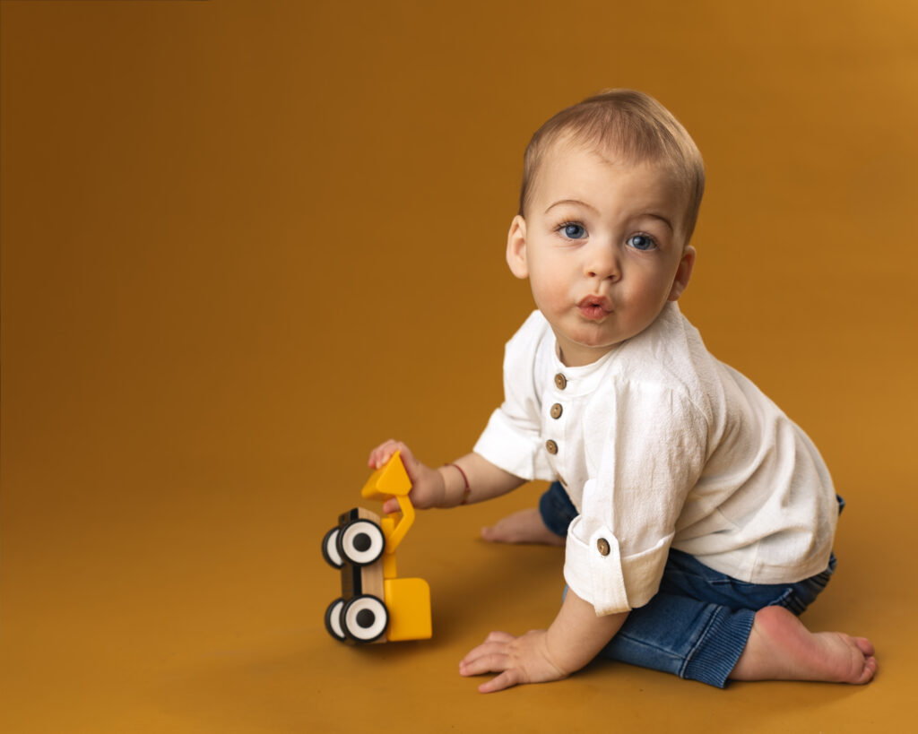 young boy playing with a toy excavator on a matching yellow backdrop