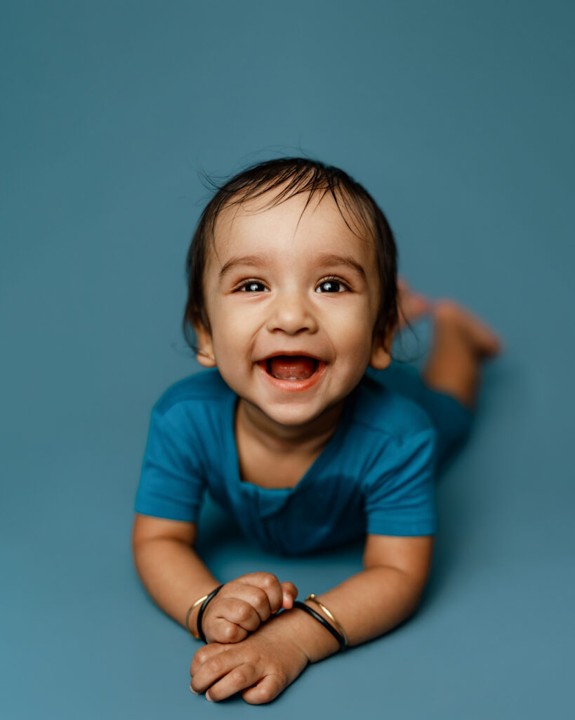 Vibrant Blue Colors in a Studio Photography Setting of a baby boy smiling on his belly