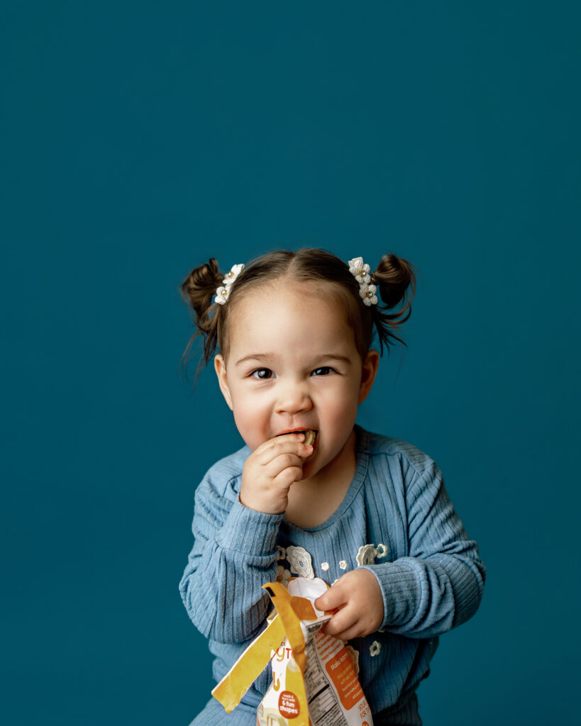 playful image of a young girl eating snacks wearing blue on a colorful blue studio backdrop