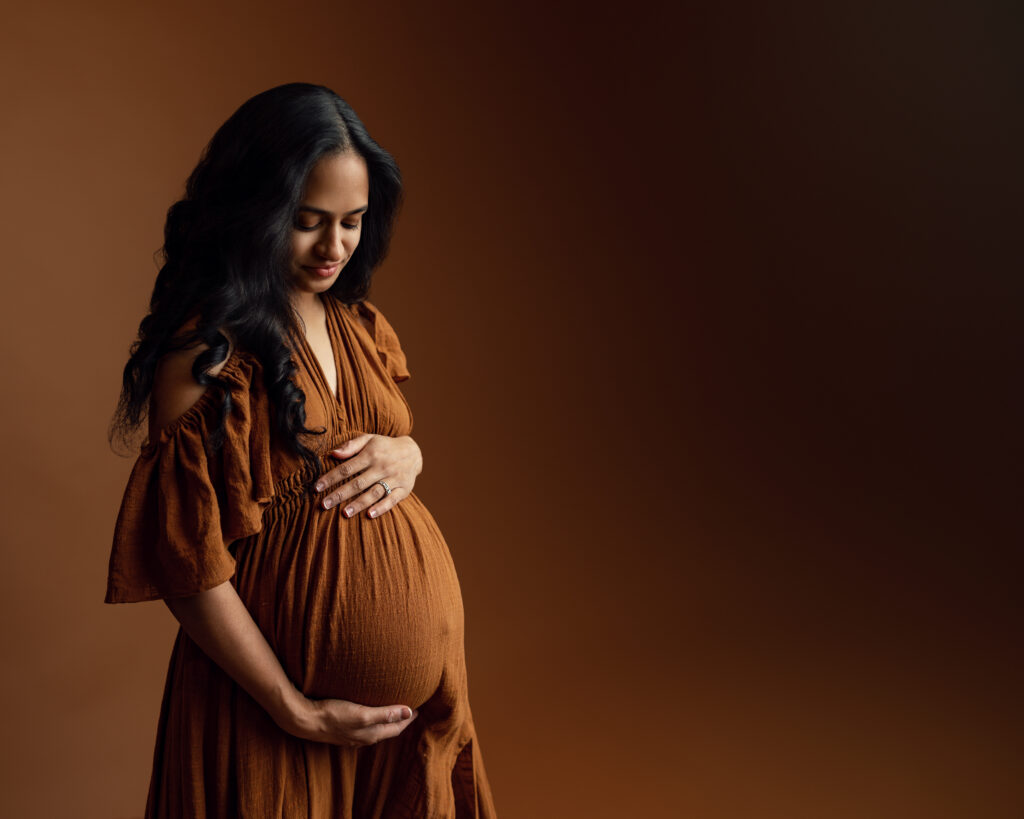 Pregnant woman wearing deep brown colors in a studio photography setting
